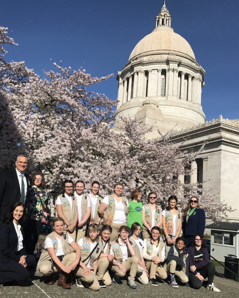 Teenagers in Girl Scout uniforms pose for a picture in front of the Capitol Building.