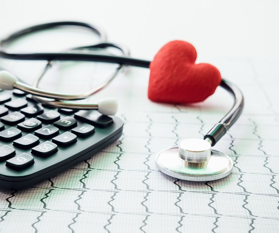 A red, felt heart rests on a stethoscope on top of a cardiogram. A calculator is just out of focus on the left.