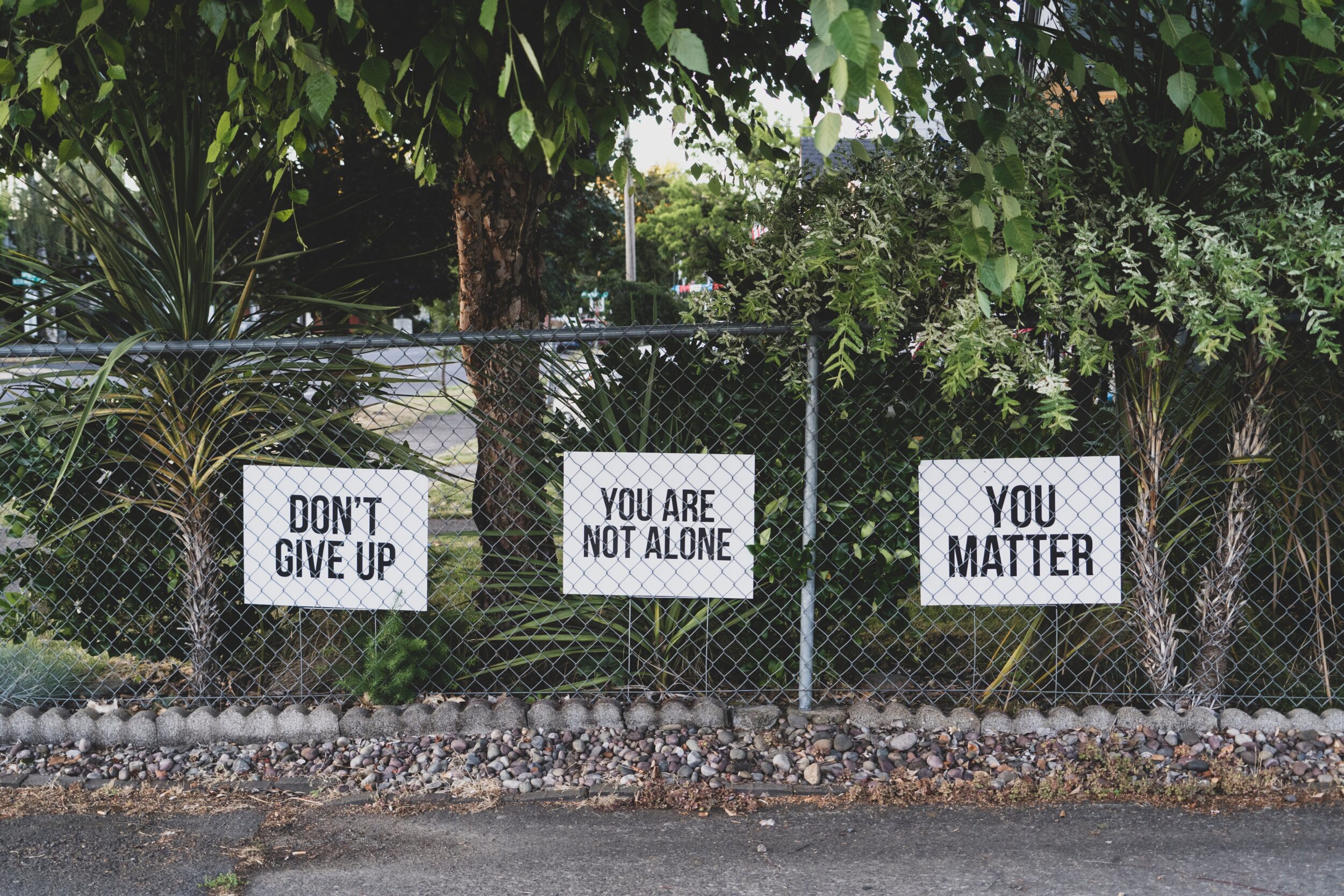 Image of a fence with signs saying "don't give up, you are not alone, you matter"